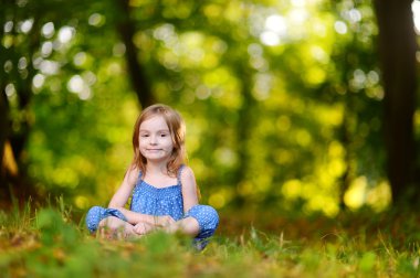 Çimenlerin üzerinde oturan sevimli küçük kız