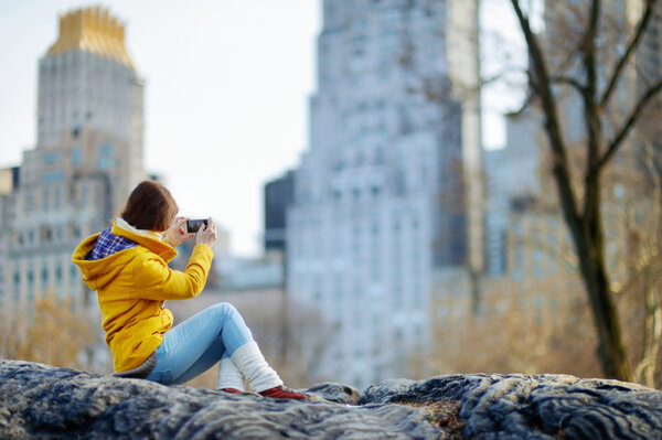 Beautiful young woman taking photo of skyscrapers in Central Park, New York