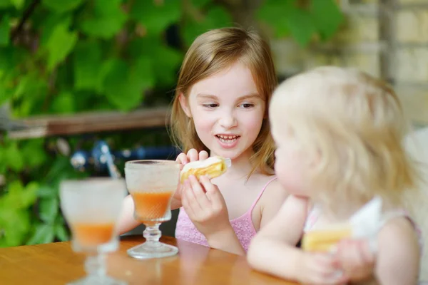Little sisters drinking orange juice — Stock Photo, Image