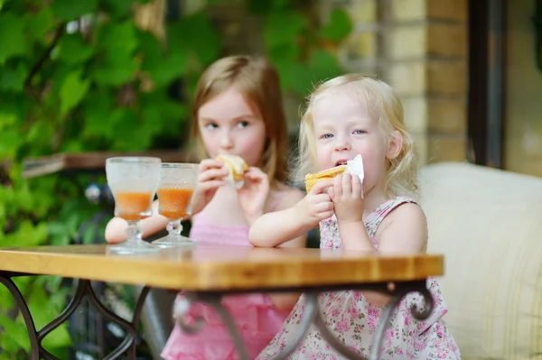 Little sisters drinking orange juice — Stock Photo, Image