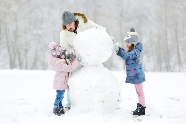 Vader en dochters bouwen sneeuwpop — Stockfoto