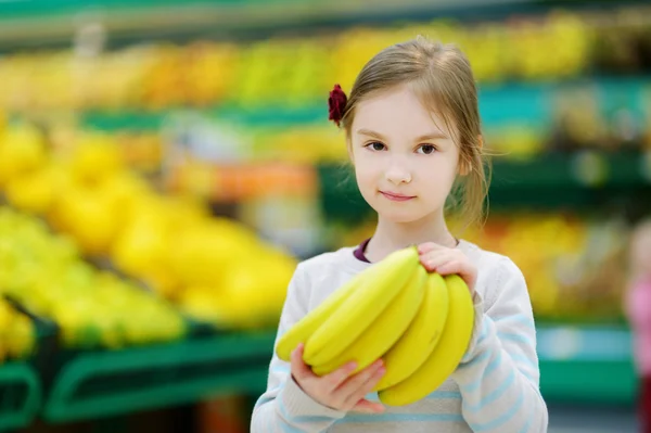 Liten flicka med bananer i butik — Stockfoto