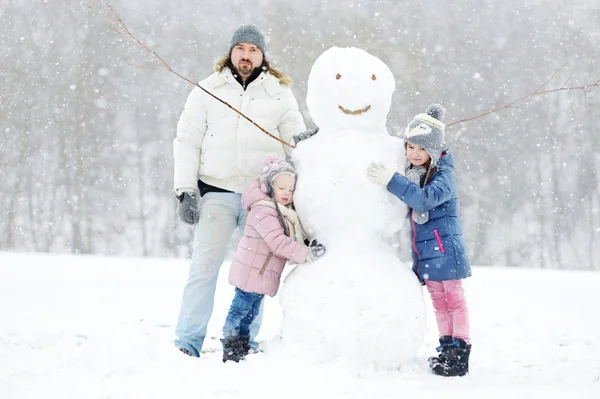 Far och döttrar bygga snögubbe — Stockfoto