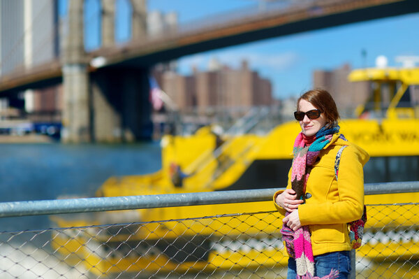 Beautiful young woman sightseeing by Brooklyn Bridge, New York, at sunny spring day
