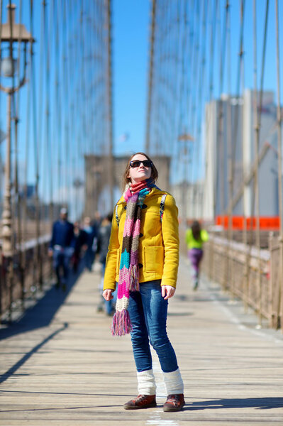 Beautiful young woman sightseeing on Brooklyn Bridge, New York, at sunny spring day