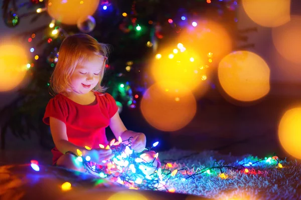 Kleines Mädchen spielt mit Weihnachtsbeleuchtung — Stockfoto