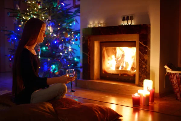 Mulher tomando uma bebida por uma lareira em um no Natal — Fotografia de Stock