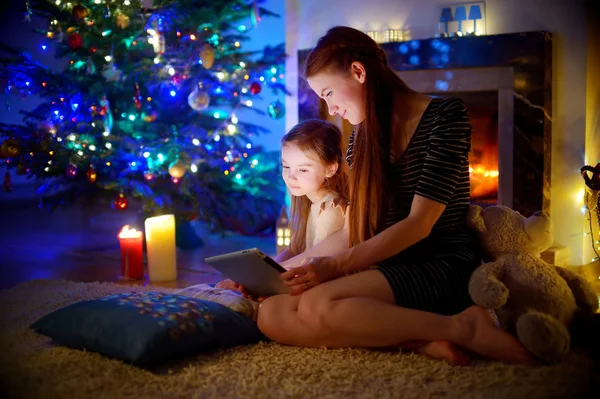 Moeder en dochter met behulp van een tablet door een open haard — Stockfoto