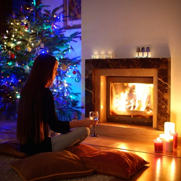 Mujer tomando una copa junto a una chimenea en una en Navidad — Foto de Stock