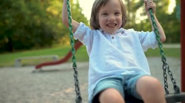 Parlak güneşli bir yaz gününde oyun alanında eğlenen sevimli küçük çocuk. Salıncaktaki sevimli çocuk. Çocuklu aileler için açık hava aktiviteleri.