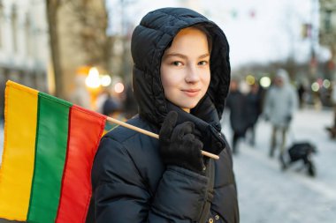 Bağımsızlık Günü kutlamaları sırasında elinde Litvanya bayrağı tutan siyah kışlık ceketli bir kız. Şubat Vilnius 'un kalbinde huzurlu ve gururlu bir an..