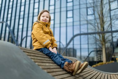 Hardal ceketli ve kot pantolonlu çocuk Vilnius 'taki bir şehir parkında modern bir ahşap binaya tırmanıyor. Kentsel kamusal alanda neşeli bir hareket ve merak anı.