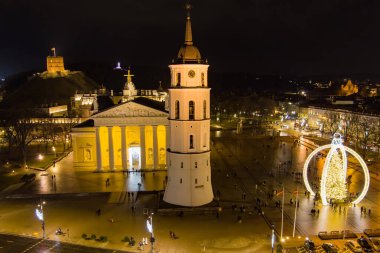 Vilnius Katedral Meydanı 'nın gökyüzü gece manzarası 2024 Noel ağacı dekoratif bir çerçevenin altında altın ışıkta parlıyor. Şehir bayramı kutlamaları sıcaklık, gelenek ve şenlik cazibesi yayıyor..