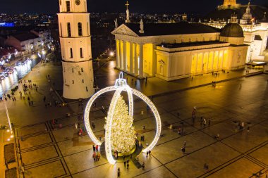 Vilnius Katedral Meydanı 'nın gökyüzü gece manzarası 2024 Noel ağacı dekoratif bir çerçevenin altında altın ışıkta parlıyor. Şehir bayramı kutlamaları sıcaklık, gelenek ve şenlik cazibesi yayıyor..