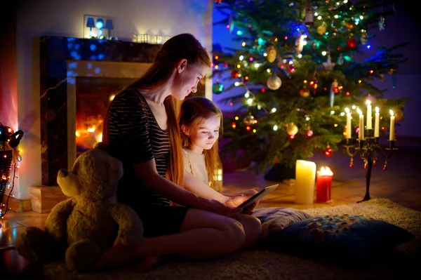 Mother and daughter using a tablet by a fireplace — Stock Photo, Image