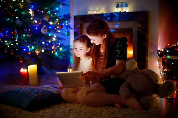 Moeder en dochter met behulp van een tablet door een open haard — Stockfoto