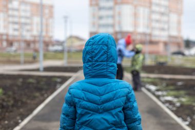 Bir çocuk, bir parkta şefkatli bir annesi olan başka bir çocuğa özlemle bakar..