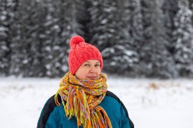 Kış manzarasının arka planında mutlu, yaşlı bir kadının portresi, kış mevsiminde yaşlı bir insanın sağlıklı yaşam tarzı..