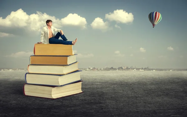 Young man sitting on books — Stock Photo, Image