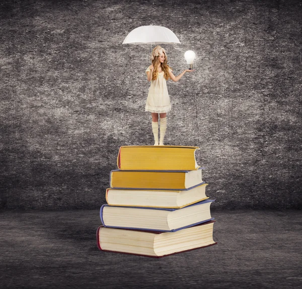 Mädchen mit Glühbirne auf Bücherstapel. — Stockfoto