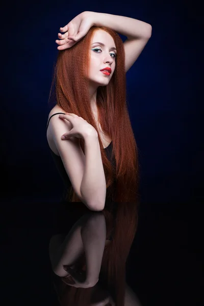 Young woman with ginger hair over reflection mirror on blue back