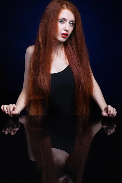 Young woman with ginger hair over reflection mirror on blue back