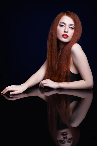 Young woman with ginger hair over reflection mirror on blue back