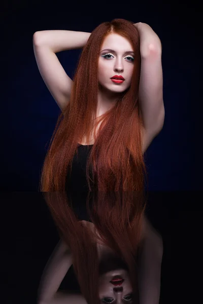 Young woman with ginger hair over reflection mirror on blue back