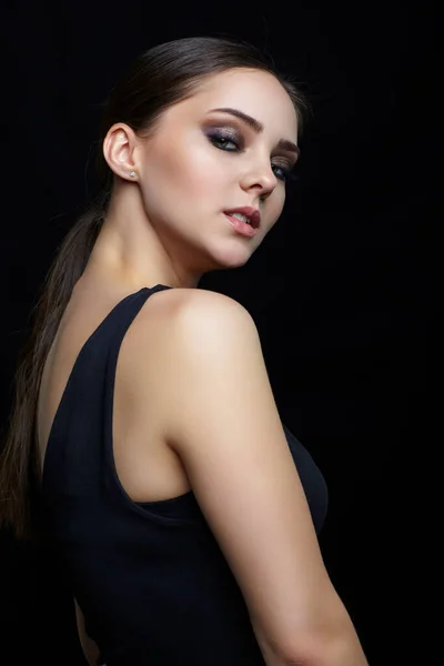 Beauty portrait of young woman on black background. Brunette girl with evening female makeup and black dess.