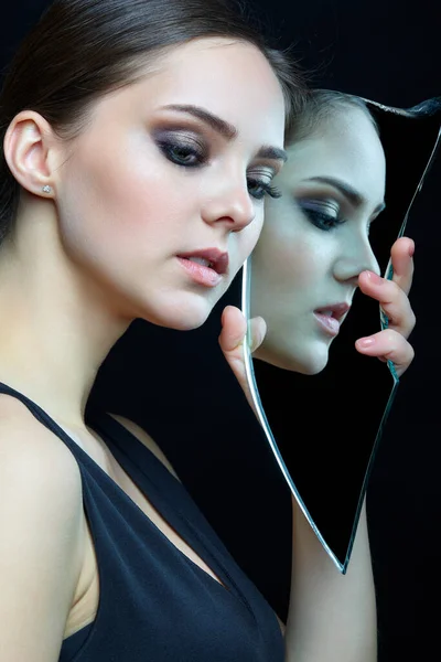 Girl with a shard of the mirror. Female with mirror shard in hand posing on gray background. Face reflection in mirror splinter.