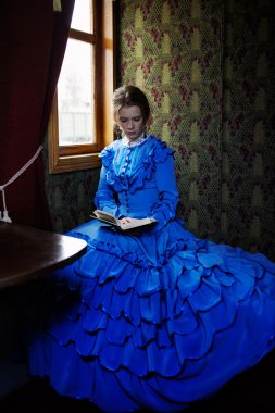 Young woman in blue vintage dress reading the book in coupe of r