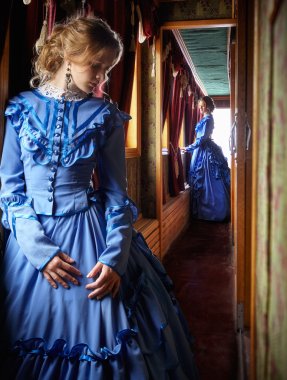 Young woman in blue vintage dress standing in corridor of retro