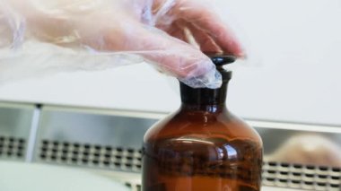 Araştırmacı siyah bir cam şişeyi kimyasal bir reaksiyonla açıyor.