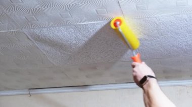 Tavanı tekerlekli fırçayla boyayan adamın yakın plan görüntüleri.