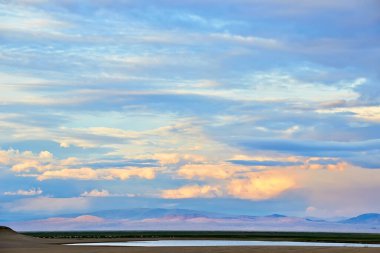 Kum tepelerinin üzerinde akşam bulutlu gökyüzü. Batı Moğolistan, Moğol-El Çölü.