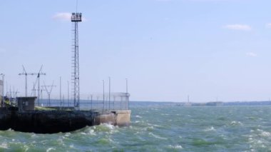 Beton iskele ve deniz dalgaları parlak güneş ışığında hareket ediyor.