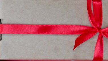 Kırmızı kurdeleli ve fiyonklu bir hediyenin yakın çekim videosu.
