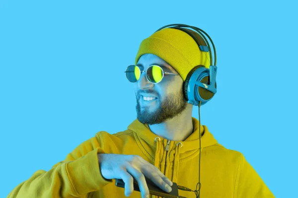 Close up portrait of funky young bearded hipster men in headphone and sunglasses. DJ in hoodie listening streaming music in smartphone player app. Rave music nightclub party concept. Copy space. — Stock Photo, Image