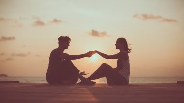 Genç çift gündoğumu arka plan üzerinde yoga yapıyor.