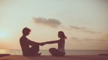 Genç çift gündoğumu arka plan üzerinde yoga yapıyor.