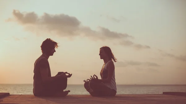 Casal jovem está fazendo ioga no fundo do nascer do sol . — Fotografia de Stock