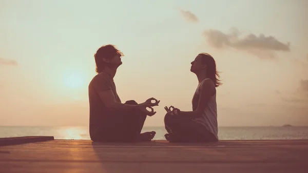 Young couple is doing yoga on the sunrise background. — Stock Photo, Image