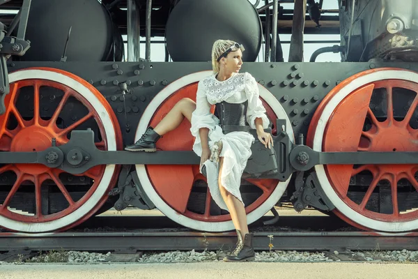 ヴィンテージのドレスを着た女性は機関車の車輪の上に座ってください。. — ストック写真