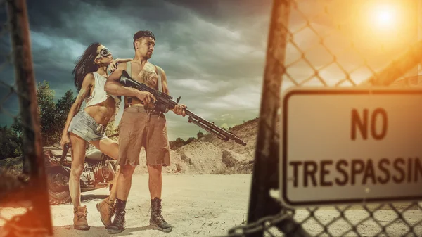 Sexy couple of bikers with the machine gun entering forbidden area — Stock Photo, Image