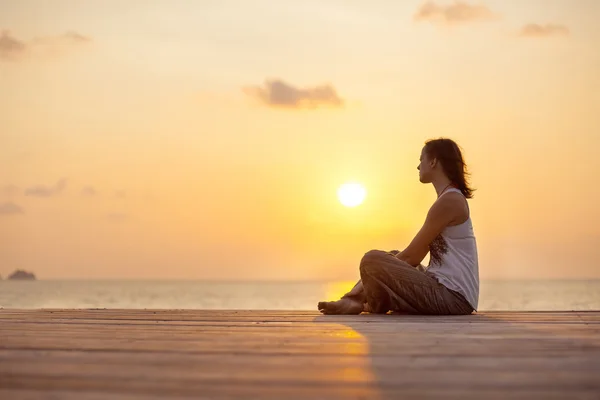 Jovem está fazendo ioga no fundo do nascer do sol . — Fotografia de Stock