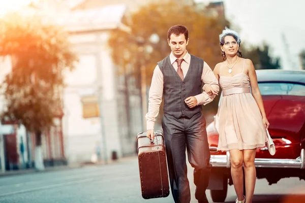 ビンテージ車の背景にスーツケースを持ってかなり歩きカップル — ストック写真
