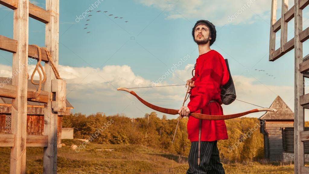 Russian archer with the wooden bow in traditional red suit and f