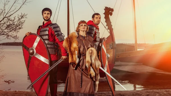 Slavic princess and two warriors with swords and shields on the warships background. — Stock Photo, Image