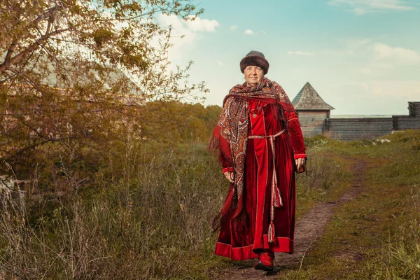 Vintage severní babička v červených šatech a šátek na dřevěné f — Stock fotografie