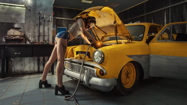 Sexy žena je svařování něco uvnitř staré auto. — Stock fotografie